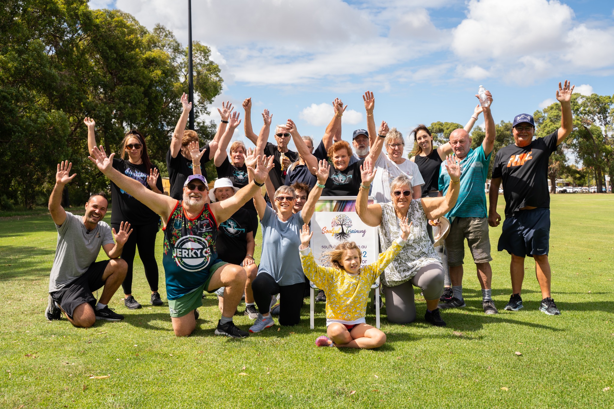 Soulful Training members and their coach smiling and waving together in a sunny park